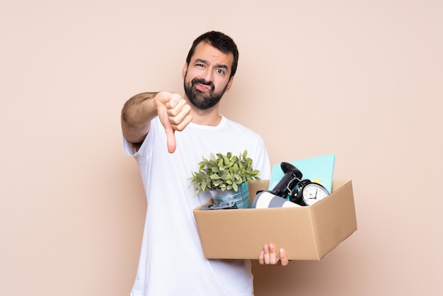 Man holding a box and moving in new home over isolated  showing thumb down with negative expression