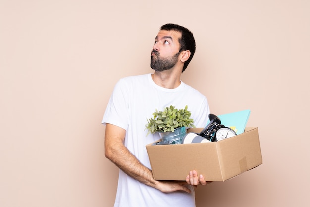 Man holding a box and moving in new home making doubts gesture while lifting the shoulders