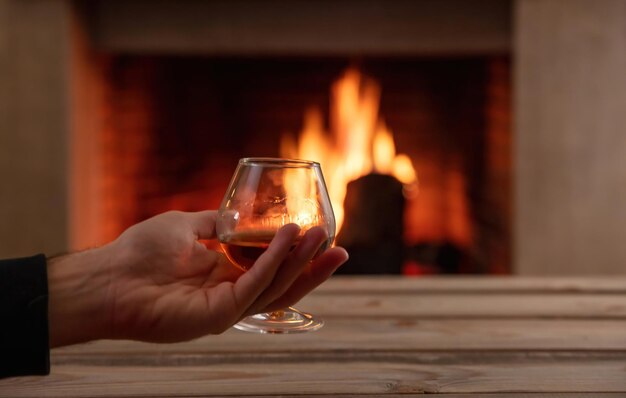 Man holding a brandy glass on burning fireplace background\
drink alcohol and relax winter time