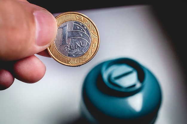 a man holding a brazil coin to save money in the penny box