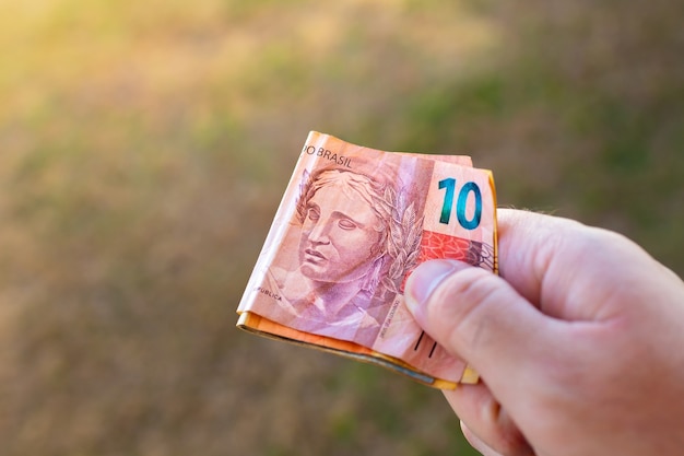 A man holding Brazilian Real bills in his hand that are folded