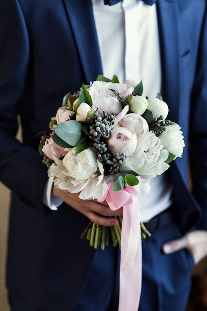 Man holding bridal bouquet in hands, groom getting ready in the morning before wedding ceremony