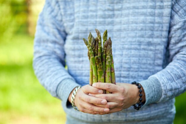 Uomo che tiene un mazzo di asparagi verdi nelle sue mani all'aperto spears of fresh asparagi verdi al sole copia spazio per il testo harvest pronto a cucinare una sana dieta vegana cibo locale