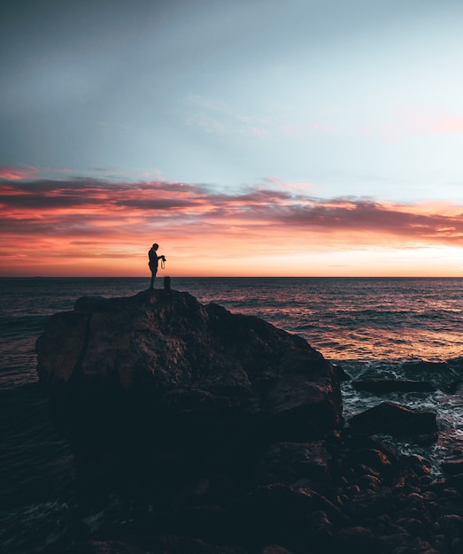 Man holding a camera in the top of a rock with a sunset