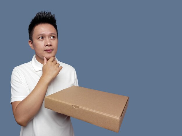 Man holding cardboard box and finger holding chin isolated on plain background