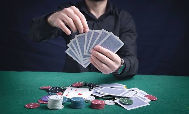 Uomo che tiene le carte con fiches del casinò sul tavolo verde.