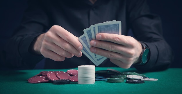 Man holding cards with casino chips on the green table.