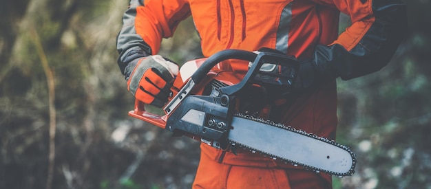 Foto uomo che tiene una motosega e taglia alberi taglialegna al lavoro giardiniere che lavora all'aperto nella foresta