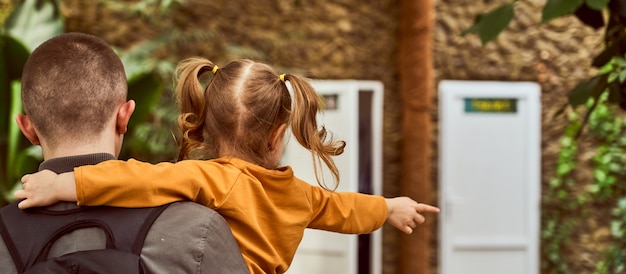 A man holding a child in his arms, back in the frame, go. the child points with a gesture