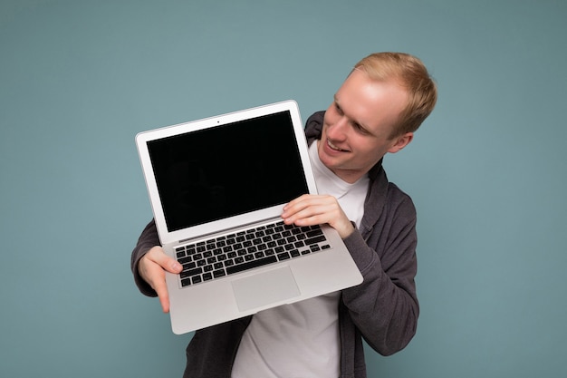 파란색 벽 위에 절연 캐주얼 옷을 입고 netbook 키보드에서 내려다보고 컴퓨터 노트북을 들고 남자.