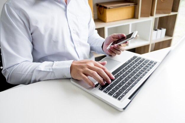 Man holding credit card in hand and entering security code using smart phone on laptop keyboard, online shopping concept