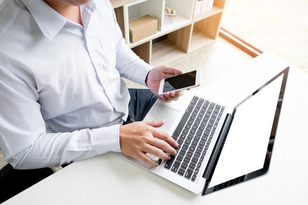 Man holding credit card in hand and entering security code using smart phone on laptop keyboard, online shopping concept