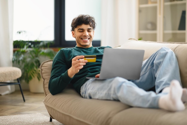 Мужчина держит кредитную карту для оплаты покупок в Интернете дома