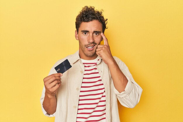 Photo man holding credit card on yellow showing a disappointment gesture with forefinger