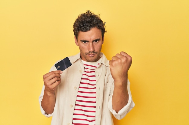 Man holding credit card on yellow showing fist to camera aggressive facial expression