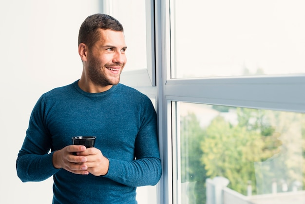 Man holding a cup of coffee and looking through the window