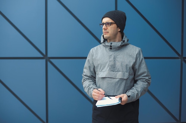 Man holding diary while looking away standing against wall