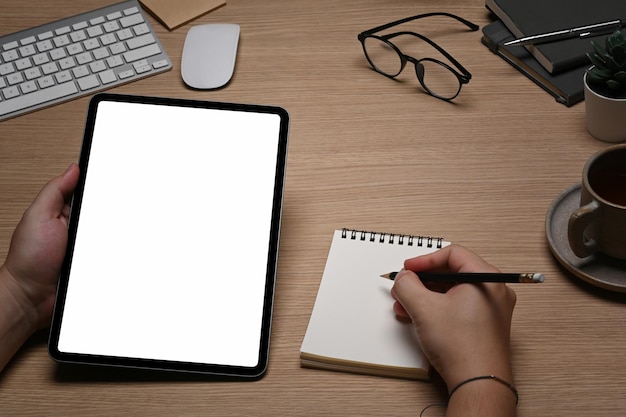 Man holding digital tablet and making notes on notebook