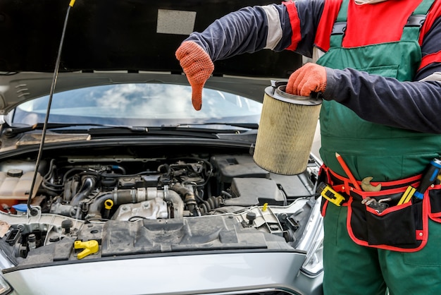 Man holding dirty filter near car at workshop