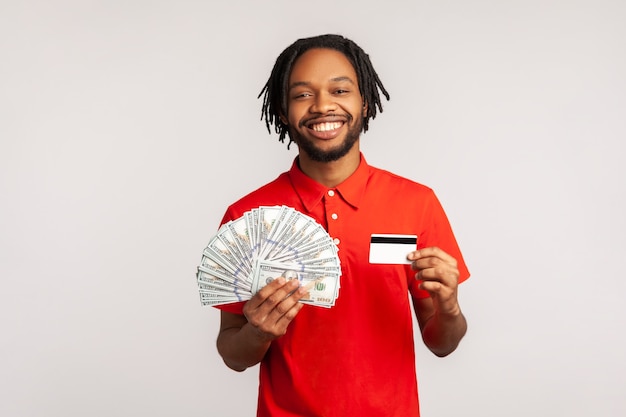 Man holding dollar bills and credit card, looking at camera with toothy smile, enjoying