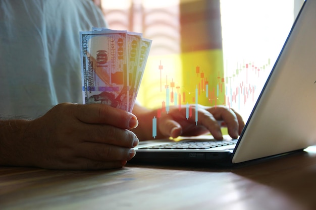 Man holding dollar in hand while using laptop ckecking information current exchange on day