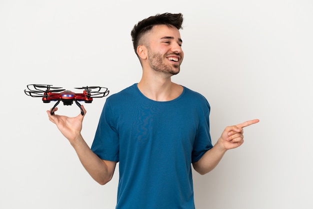 Man holding a drone isolated on white background pointing finger to the side and presenting a product