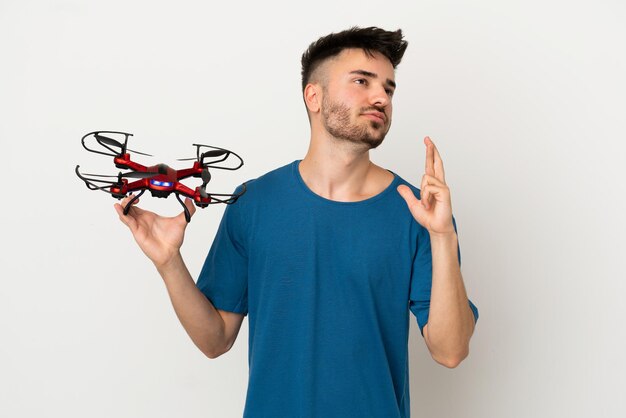 Man holding a drone isolated on white background with fingers crossing and wishing the best