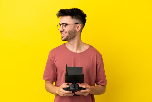 Man holding a drone remote control isolated on yellow background looking to the side and smiling