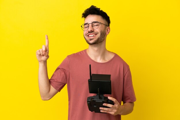 Man holding a drone remote control isolated on yellow background showing and lifting a finger in sign of the best