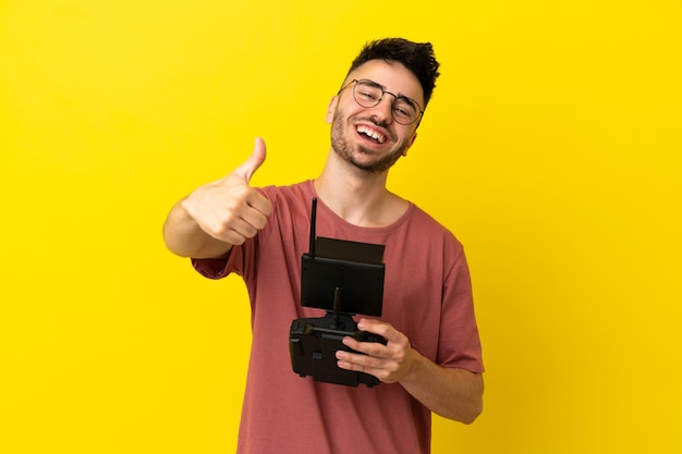 Man holding a drone remote control isolated on yellow background with thumbs up because something good has happened