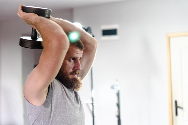 Photo man holding dumbbell while exercising at gym