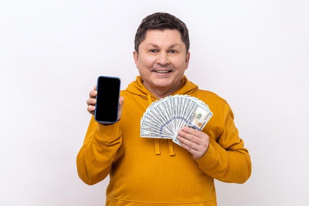 Man holding empty screen smartphone ad fan of hundred dollars looking at camera with smile