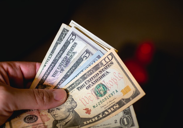 A man holding fanshaped Us dollar bills in dark environment