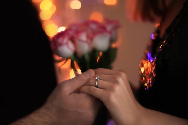 Man holding fiancees hand with engagement ring against blurred lights