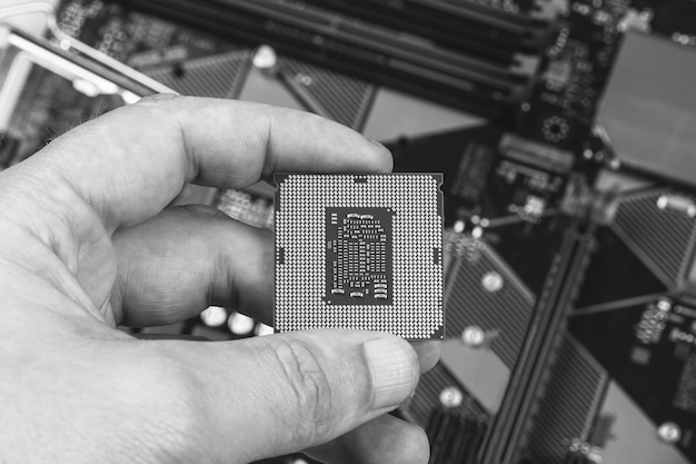 Man holding fingers desktop processor 8th gen on background motherboard closeup top view, black and white photo