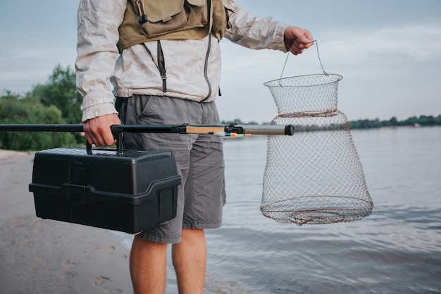 Foto uomo che tiene la rete da pesca e scatola nera di plastica in mano. anche lui ha la mosca in quella giusta. guy è in piedi sulla riva del watr.