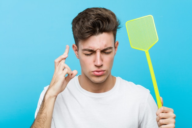 Man holding a fly swatter crossing fingers for having luck