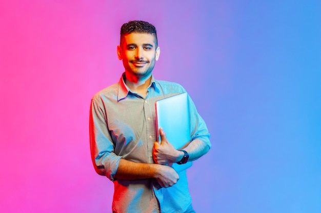 Man holding folded laptop looking at camera with happy facial expression finish work