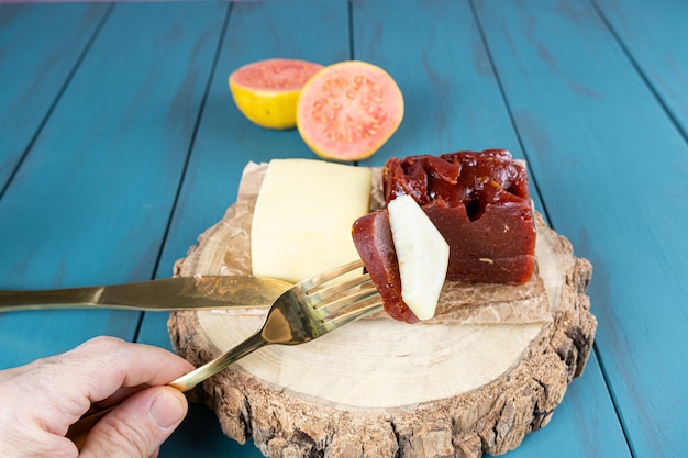 Man holding a fork with pieces of guava sweet with cheese on a wooden board