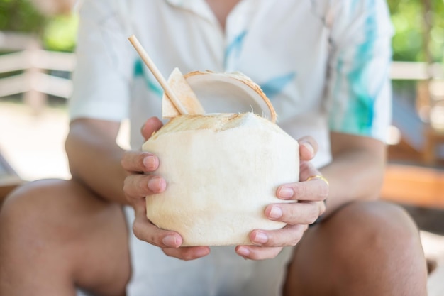 熱帯のビーチで飲んでいる間に新鮮なココナッツジュースを保持している男夏のリラックスと休暇の概念