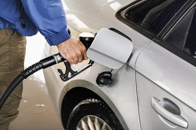 Man holding fuel nozzle, filling gas tank of diesel car covered with some rain drops