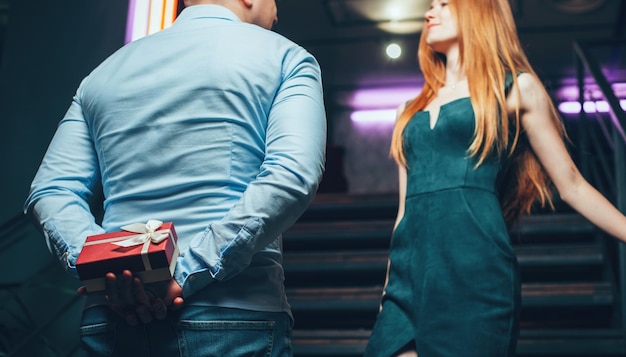 Man holding a gift on his back while congratulating his girlfriend on valentines day birthday party ...