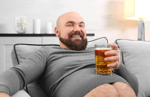 Man holding glass of beer on his big belly at home