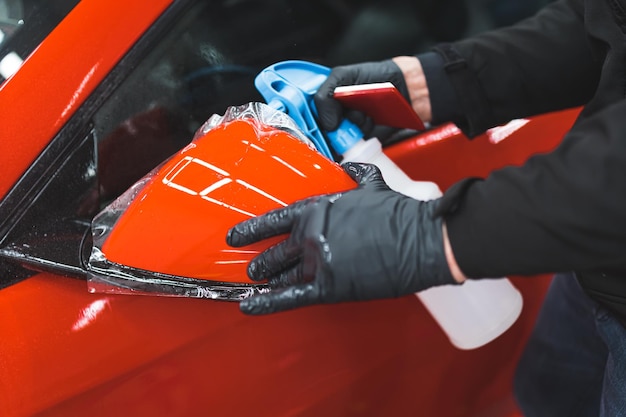 Man holding a glass cleaner and touching a cars side mirror wrapped in a vinyl film