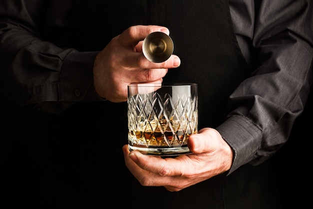 Man holding a glass of whisky and a bar jigger