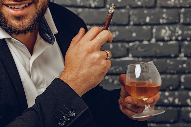 ウイスキーと火のついたタバコのグラスを手に持っている男クローズアップ写真