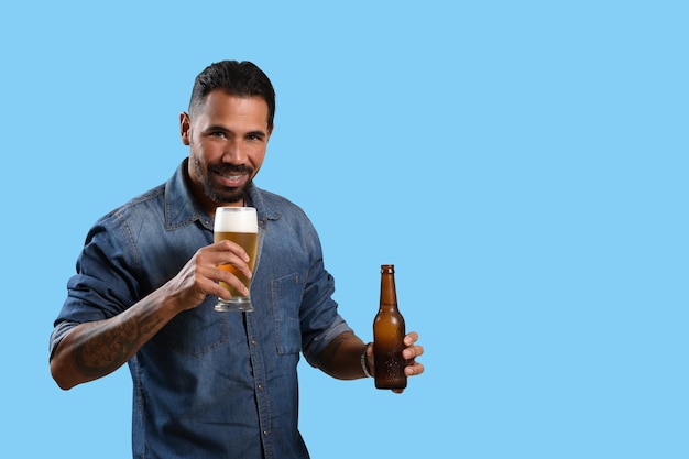 Foto uomo con un bicchiere di birra e una bottiglia di birra senza etichetta che sorride guardando la telecamera