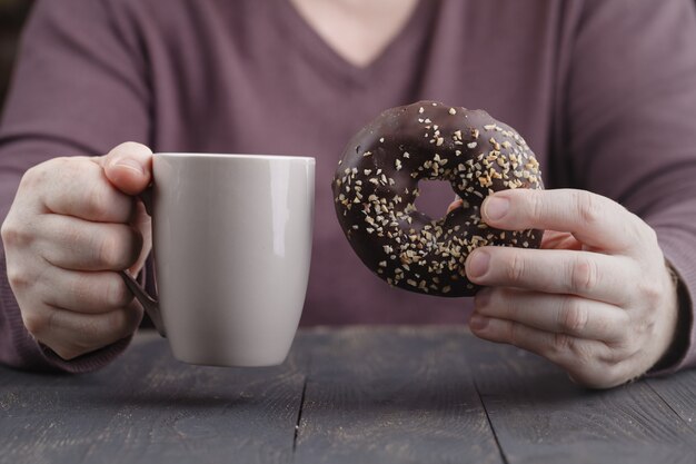 Man holding glazed donut and cup of coffee