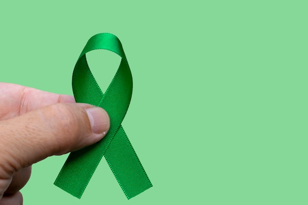 Мужчина держит зеленую ленту. Концепция месяца осведомленности рака печени, желчного пузыря, почки и лимфомы.