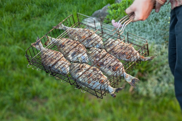 Uomo che tiene un pesce alla griglia in una griglia d'acciaio